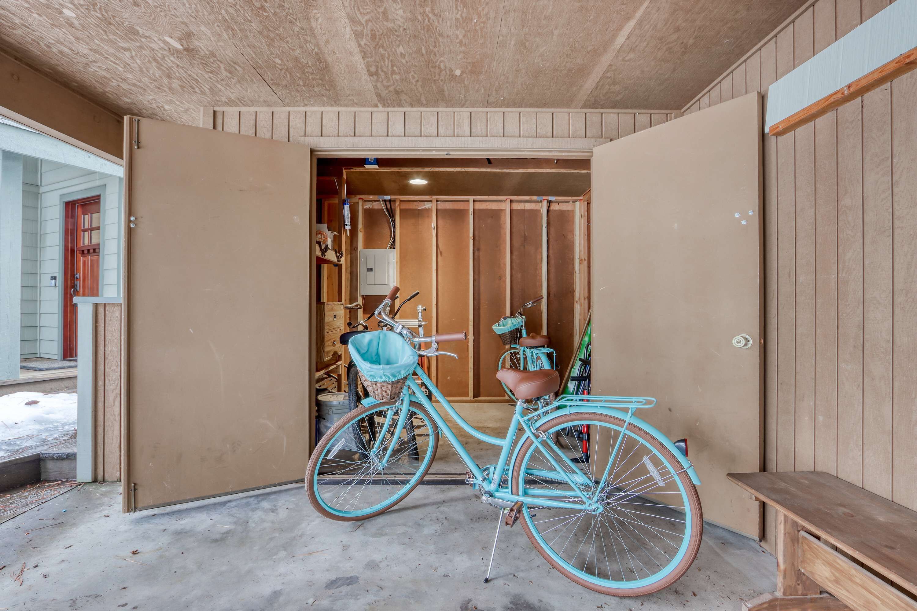 A bicycle with a basket and a seat, a wooden bench, and a partially open door leading to another room.