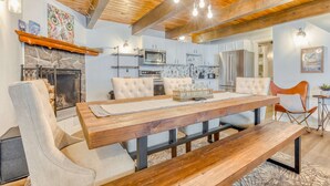Un comedor con mesa y sillas de madera, una chimenea y una cocina al fondo.