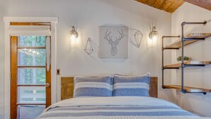 Un dormitorio con cama, puerta de madera, estantes en la pared y una obra de arte con cabeza de ciervo.