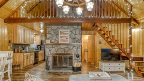 A wooden interior with a stone fireplace, a dining area, a living room with a sofa, and a staircase.