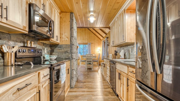 A kitchen with wooden cabinets, a stone accent wall, a stainless steel refrigerator, and a central island with seating.