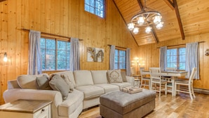 A wooden interior with a sofa, ottoman, dining table, chairs, and a chandelier.