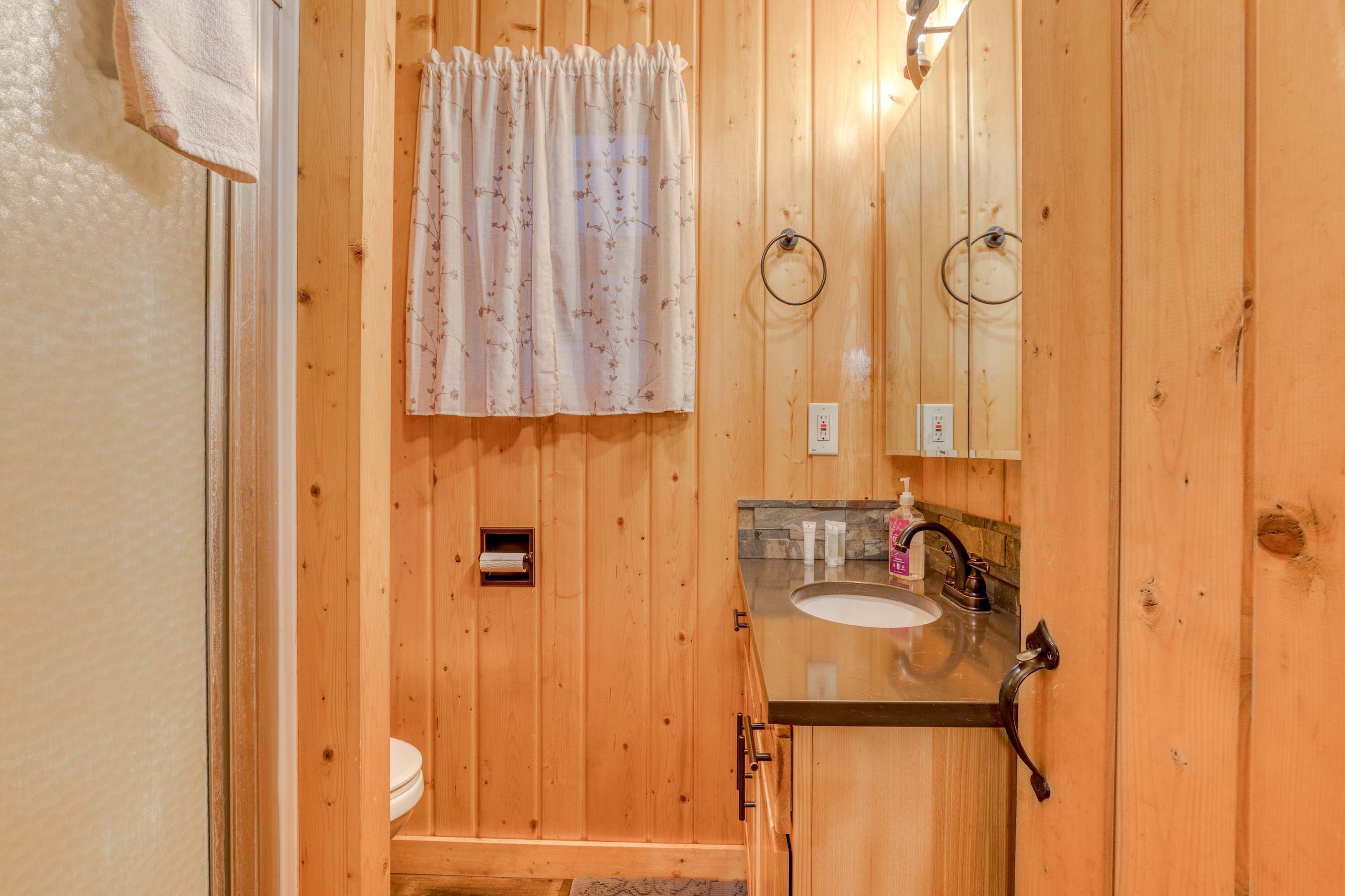 A wooden bathroom with a toilet, sink, and mirror.