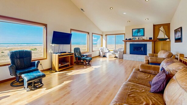 Amplia sala de estar con ventanas grandes, chimenea, televisor y un área de estar acogedora.