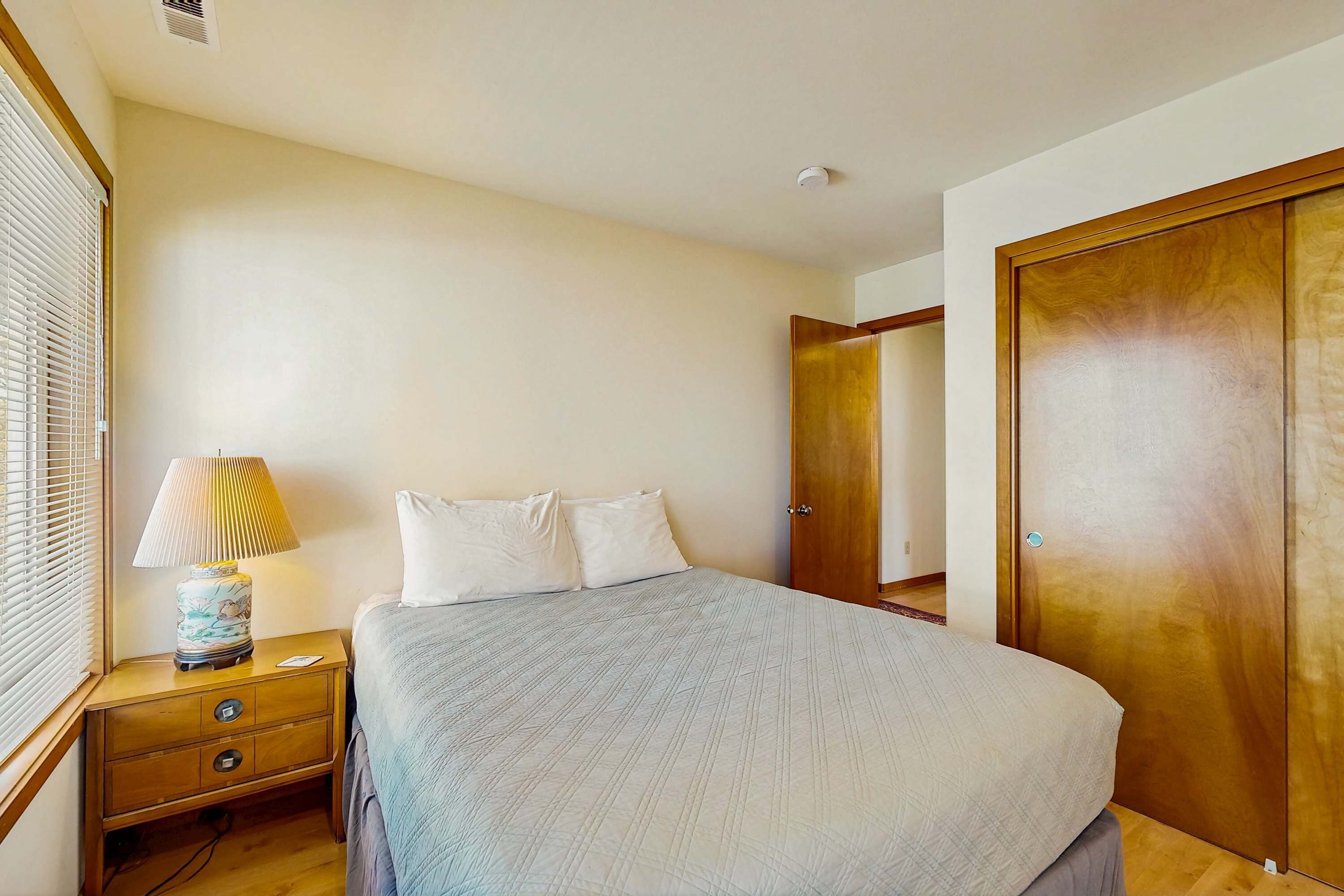 A bedroom with a bed, nightstand, lamp, and wooden wardrobe.