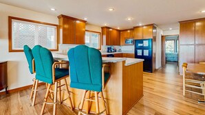 Una cocina moderna con armarios de madera, una isla central, taburetes de bar color aguamarina y un comedor.