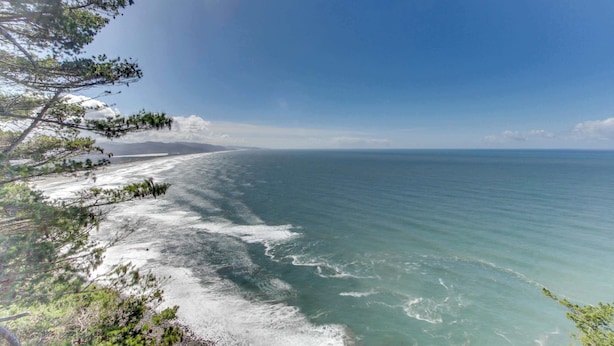 Eine Küstenlandschaft mit blauem Himmel, Sandstrand und ruhiger See.