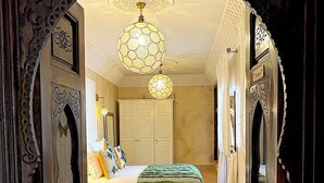 Een sierlijke deur die leidt naar een slaapkamer met een bed, een kroonluchter en vloerbedekking met een patroon.