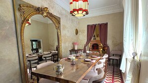 Een eetkamer met een grote, versierde spiegel, een open haard en een vloer met een patroon.