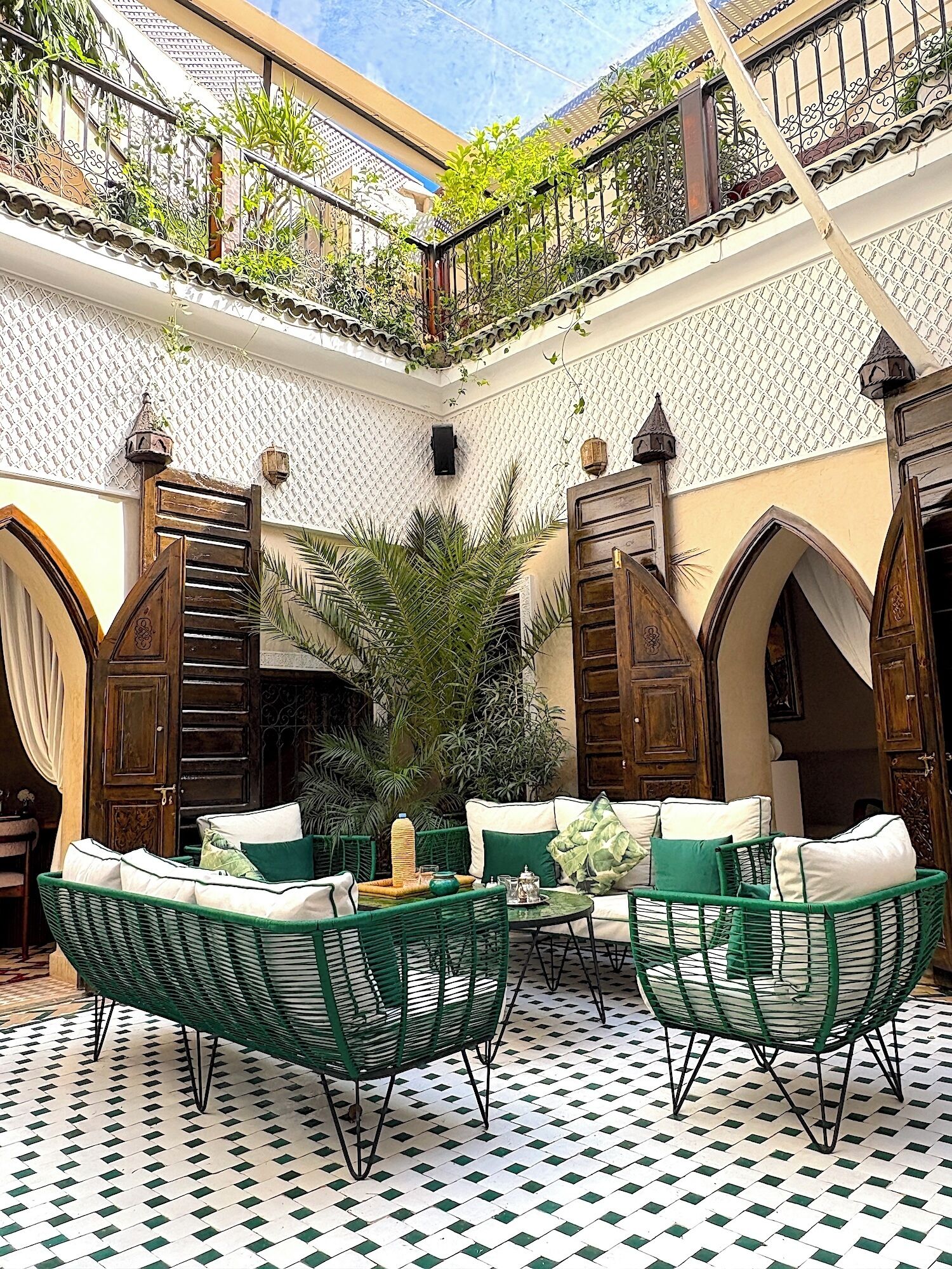 An outdoor patio with a checkered floor, green wicker furniture, and a decorative railing.