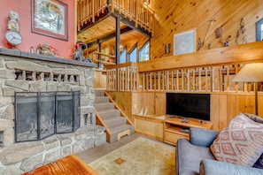 A cozy living room with a stone fireplace, wooden staircase, and a television. - Serene Wooded Retreat with Free WiFi, Large Deck & Spacious Loft - Skiing Nearby (Government Camp)
