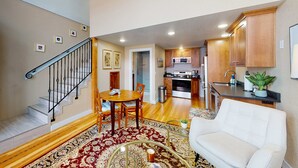 A spacious living area with a staircase, a dining table, a sofa, and a kitchen in the background.