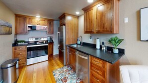 A kitchen with wooden cabinets, stainless steel appliances, a black countertop, and a patterned rug.