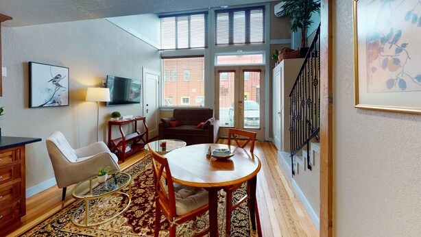 A dining area with a round table, chairs, a sofa, a TV, and a window with blinds.
