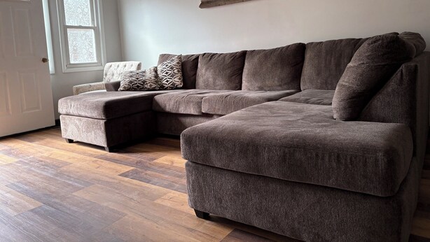 A sectional sofa with a chaise, a decorative wooden piece on the wall, and a patterned throw pillow.