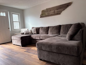 A sectional sofa with a chaise, a decorative wooden piece on the wall, and a patterned throw pillow.