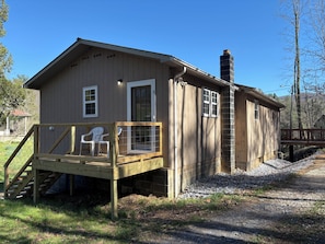 A wooden cabin with a deck, a chimney, and a small porch with chairs.