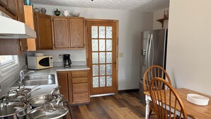 A kitchen with wooden cabinets, a stainless steel refrigerator, a microwave, and a dining table with a chair.