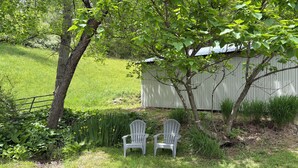 A grassy outdoor area with two white chairs, a tree, and a shed.