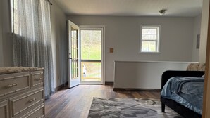 A bedroom with a bed, a dresser, a patterned rug, a window, and a door leading outside.