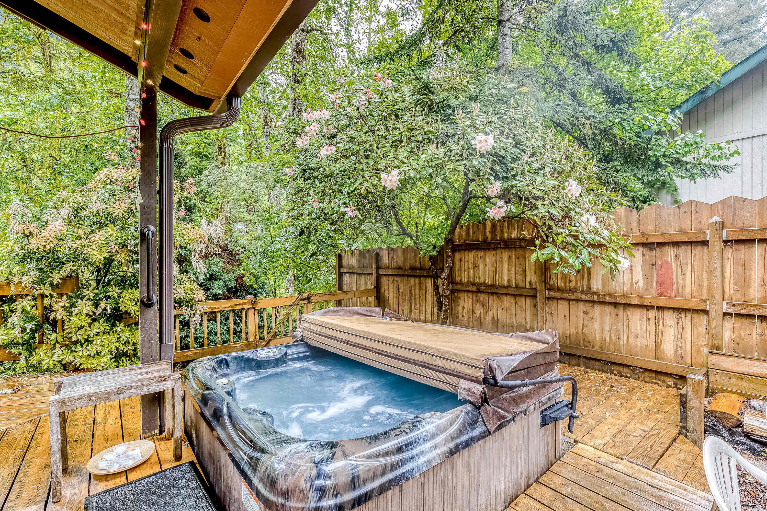 Un bain à remous sur une terrasse en bois, entouré d’une clôture en bois et d’une végétation luxuriante.