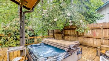 Un bain à remous sur une terrasse en bois, entouré d’une clôture en bois et d’une végétation luxuriante.
