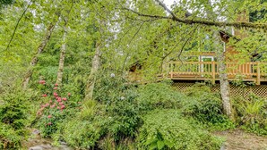 A wooden deck with a wooden fence, surrounded by dense green foliage and a small stream.