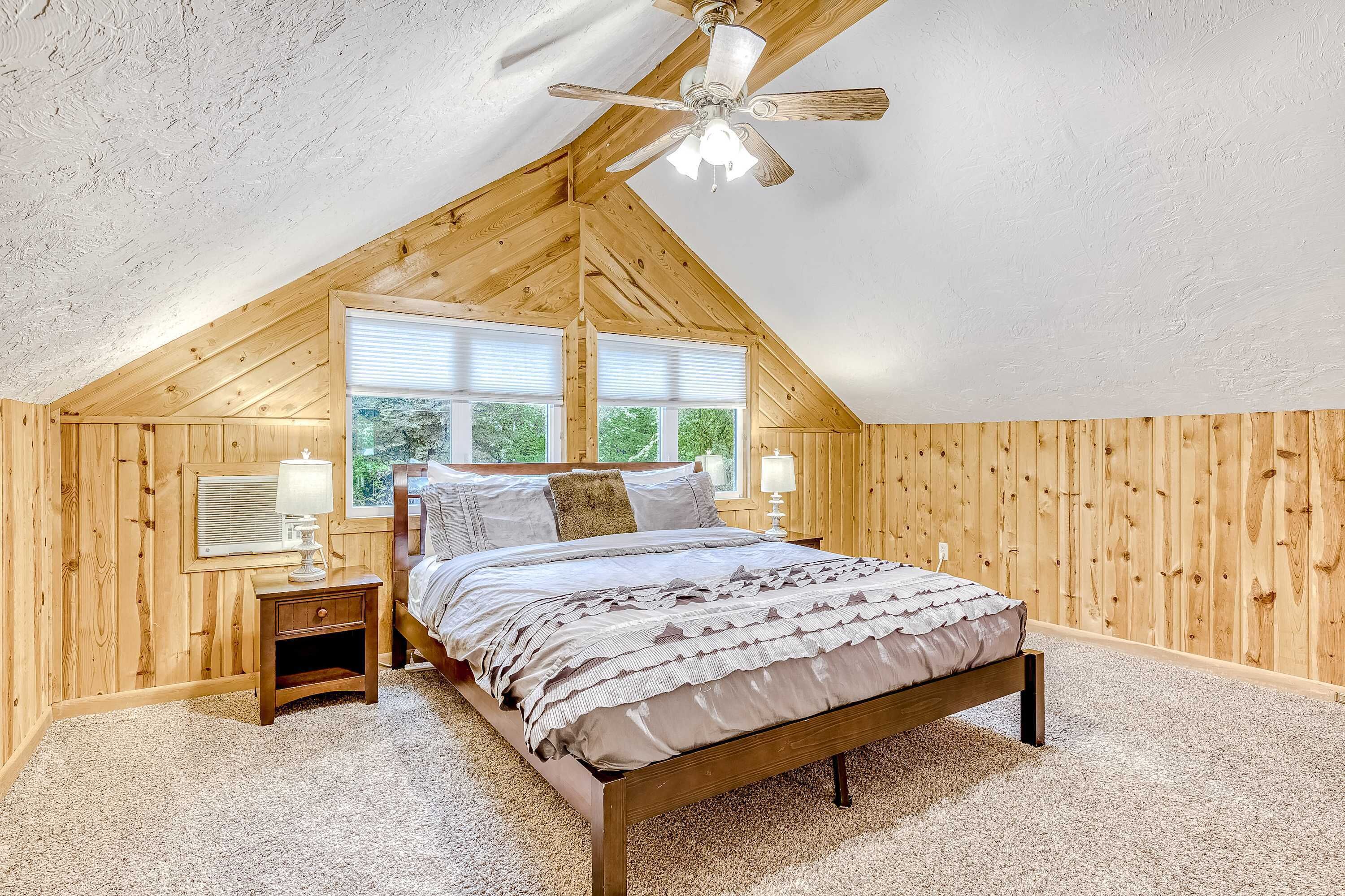 Une chambre avec un plafond en pente, un lit, une table de chevet, une lampe et une fenêtre.