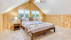 A bedroom with a sloped ceiling, a bed, a nightstand, a lamp, and a window.