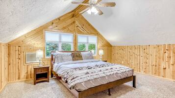 Une chambre avec un plafond en pente, un lit, une table de chevet, une lampe et une fenêtre.