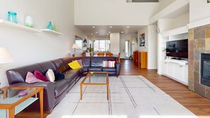A spacious living area with a sofa, coffee table, and TV. There are shelves with decorative items and a fireplace. - Spacious townhouse with fireplace, fast WiFi & resort pools-hot tub-golf (Eagle Crest)