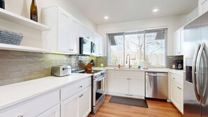 A modern kitchen with white cabinets, a stainless steel refrigerator, a dishwasher, a toaster, and a window with blinds. - Spacious townhouse with fireplace, fast WiFi & resort pools-hot tub-golf (Eagle Crest)