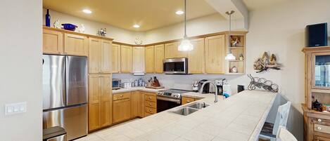 A kitchen with wooden cabinets, stainless steel appliances, a large island, and pendant lighting.
