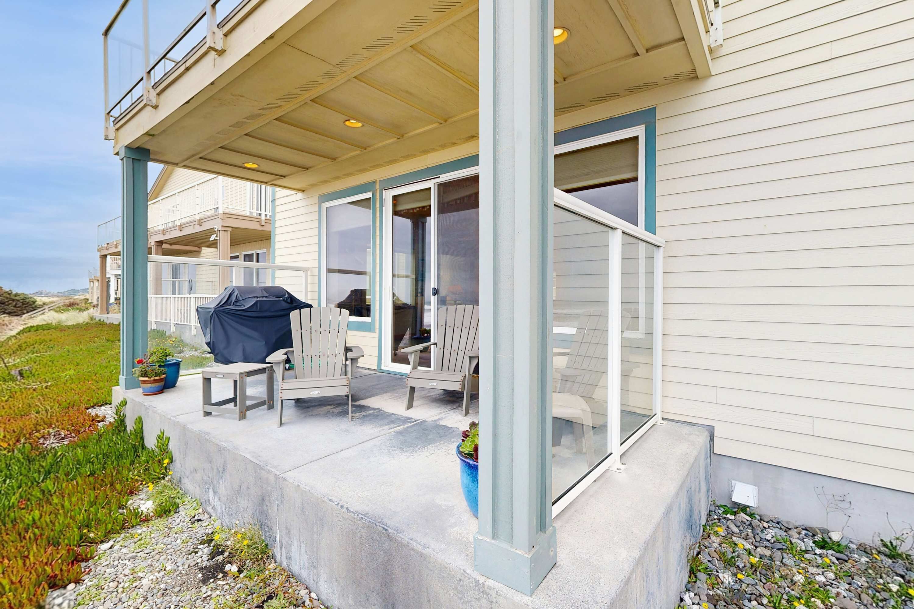 A covered outdoor seating area with chairs and a grill, a glass door leading to a covered balcony, and a concrete step leading to the entrance.