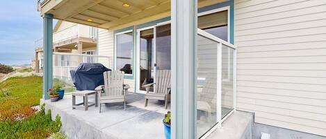 A covered outdoor seating area with chairs and a grill, a glass door leading to a covered balcony, and a concrete step leading to the entrance.