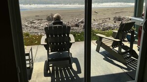Blick auf den Ozean durch ein Fenster, eine Person sitzt in einem Stuhl und blickt auf den Strand.