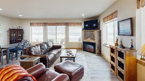 Ein Wohnzimmer mit Sofa, Couchtisch, Kamin, Fernseher und Fenstern.