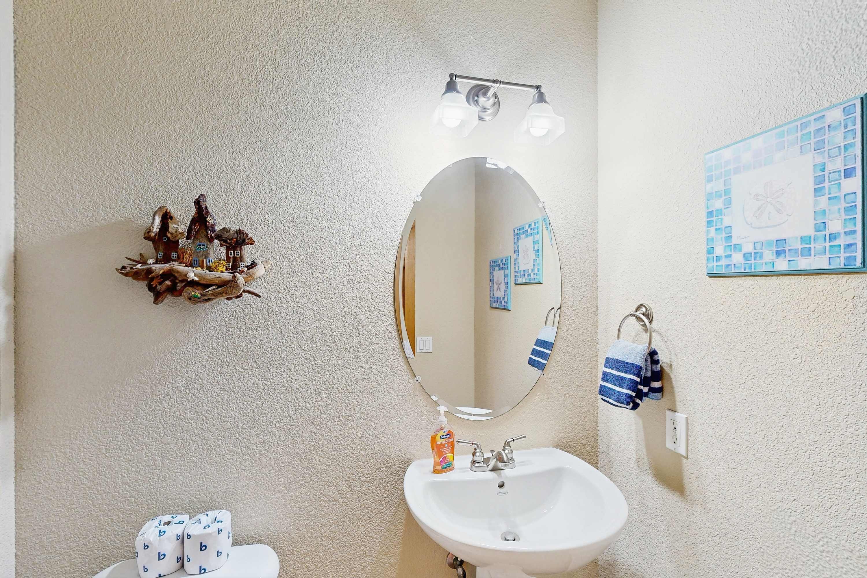 Une salle de bain avec un lavabo blanc, un miroir, un luminaire, un porte-serviettes et un élément décoratif sur le mur.