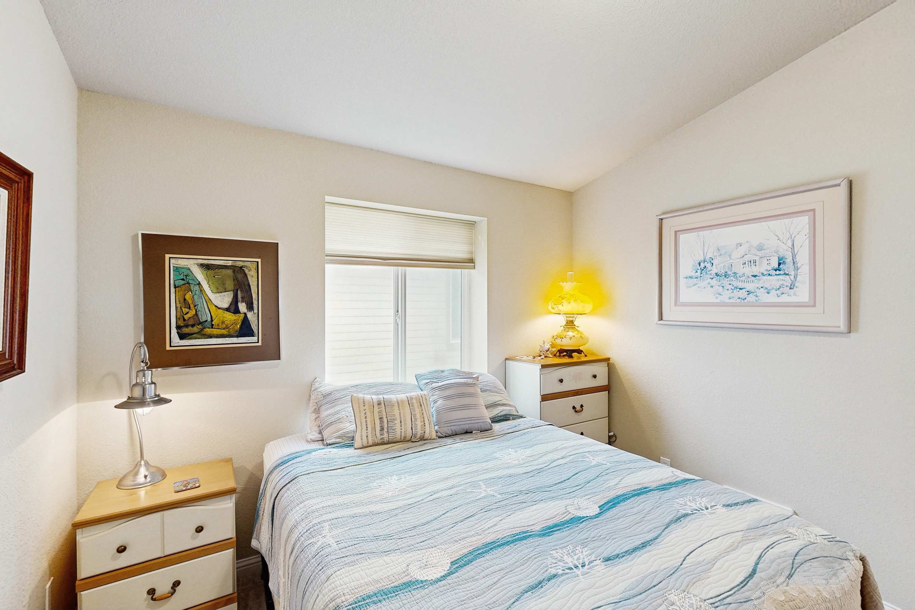 A bedroom with a bed, bedside tables, a lamp, and framed artwork on the walls.