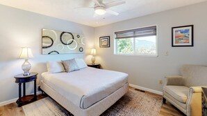 Un dormitorio con cama, dos lámparas de noche, ventilador de techo, ventana con persianas y obras de arte en las paredes.