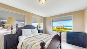 Ein Schlafzimmer mit einem Bett, zwei Nachttischen, einer Kommode und großen Fenstern mit Jalousien.