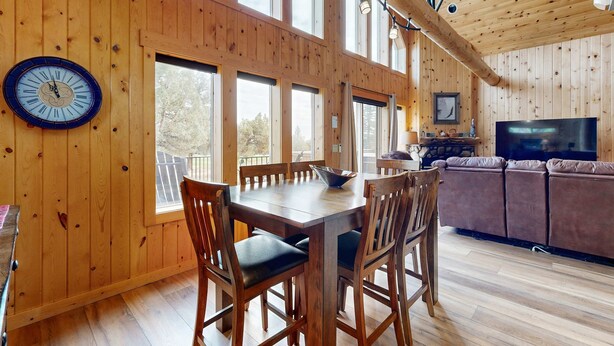 Ein Holzinterieur mit Esstisch, Stühlen, einer Couch, einem Fernseher und großen Fenstern.