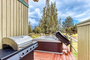 A barbecue grill and a hot tub on an outdoor deck with a wooden fence and trees in the background. - Beautifully updated, golf-course-front chalet with deck, pools, hot tubs & gyms (Eagle Crest)