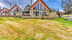 Eine Reihe von Holzhütten mit einer Holzterrasse und einem überdachten Bereich, eingebettet in eine grüne Wiese mit Bäumen im Hintergrund.