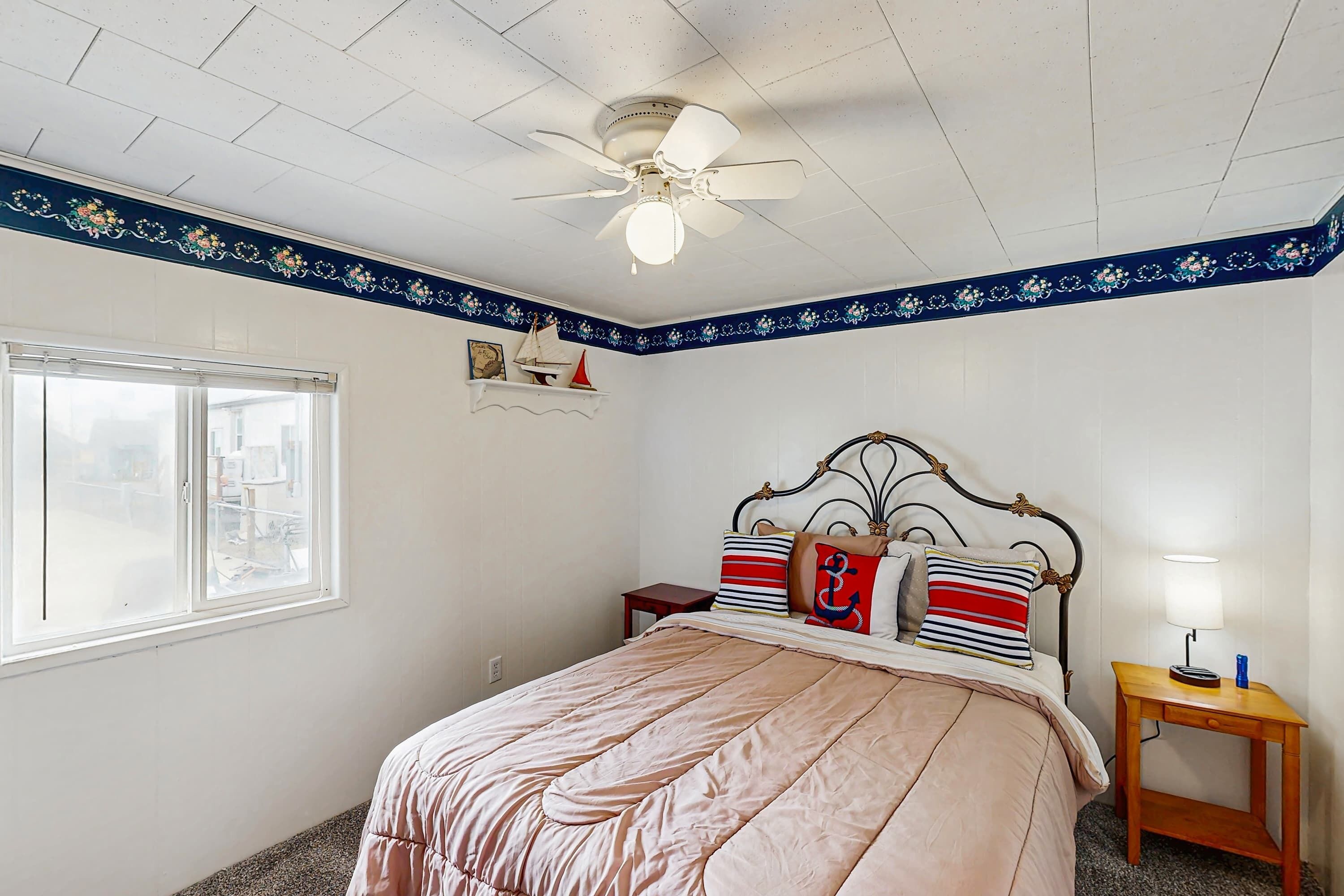 A bedroom with a bed, a nightstand, a ceiling fan, a window, and a decorative border on the wall.