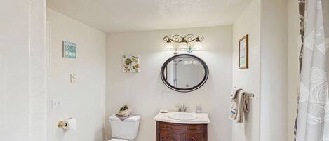 A bathroom with a toilet, sink, vanity, mirror, and shower curtain.