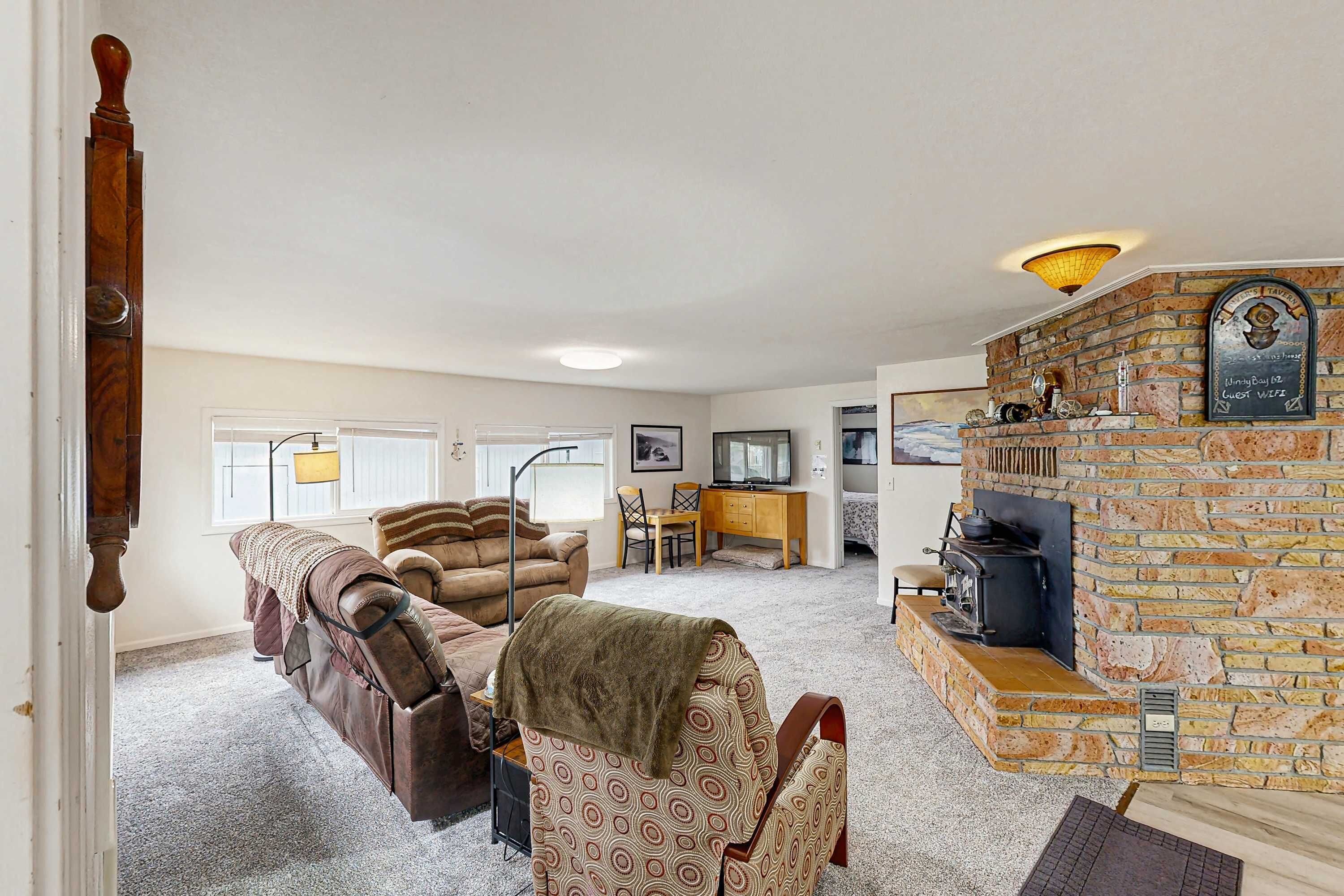 A living room with a fireplace, a sofa, a patterned armchair, a dining area, and a television.