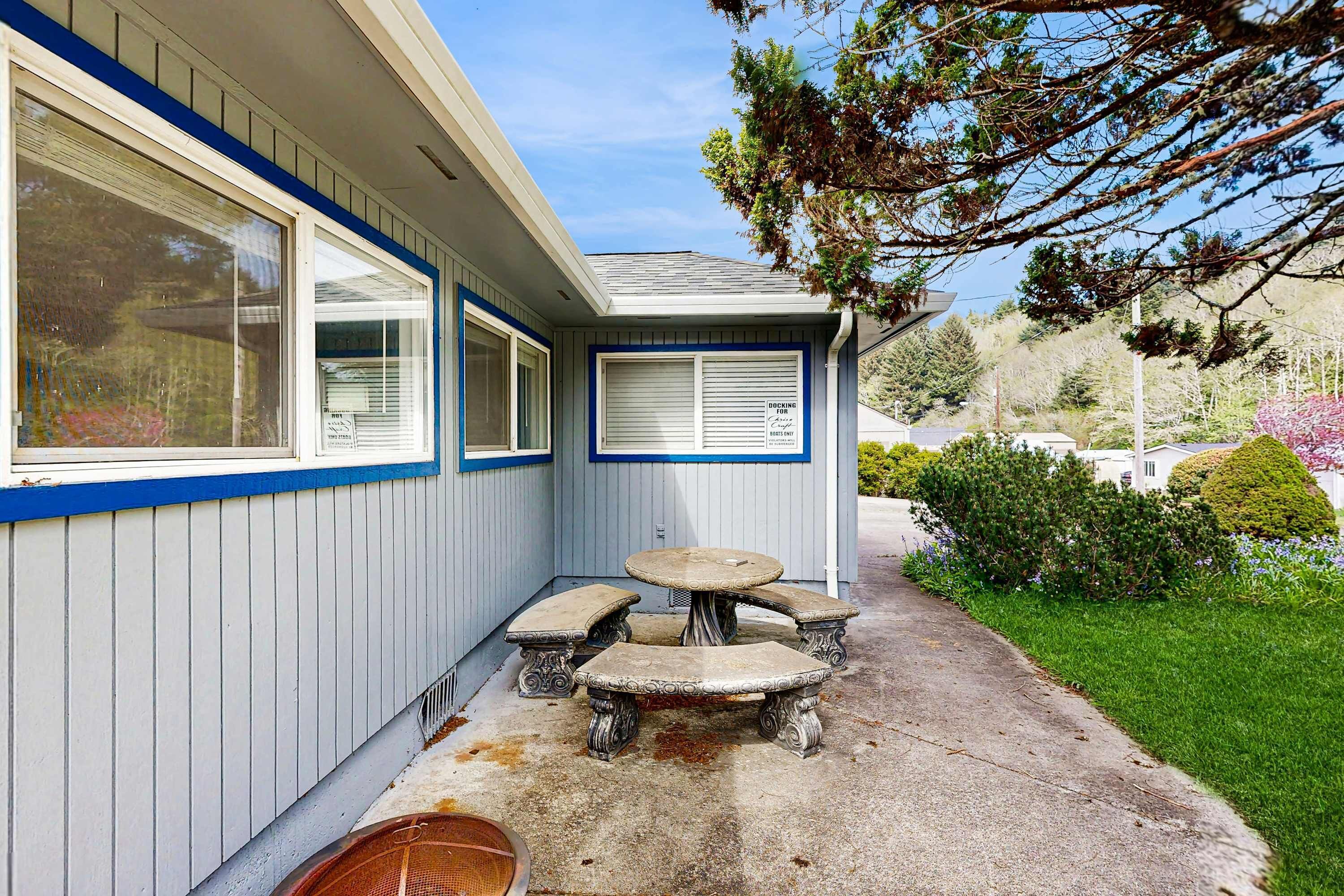 Un bâtiment à la façade bleue, une terrasse couverte avec une table et des bancs, et une fenêtre sur laquelle est apposée une enseigne.