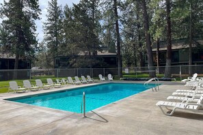 A swimming pool with lounge chairs, surrounded by trees and a fenced area.