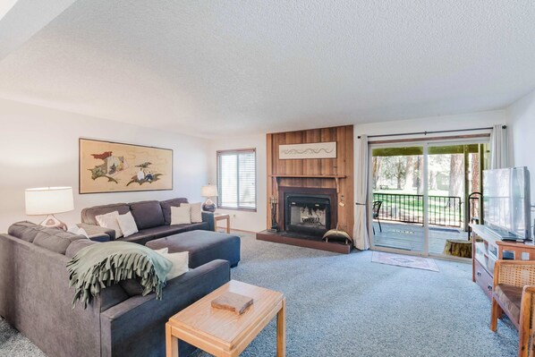 A living room with a fireplace, a sofa, a television, and a balcony with a view of trees. - Delightful escape near downtown with shared pool & hot tub, rec room, & large deck (Sisters)